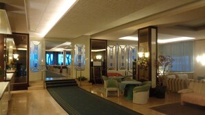 Een ruime woonkamer met een lang blauw tapijt, een trap en uitzicht op een balkon.