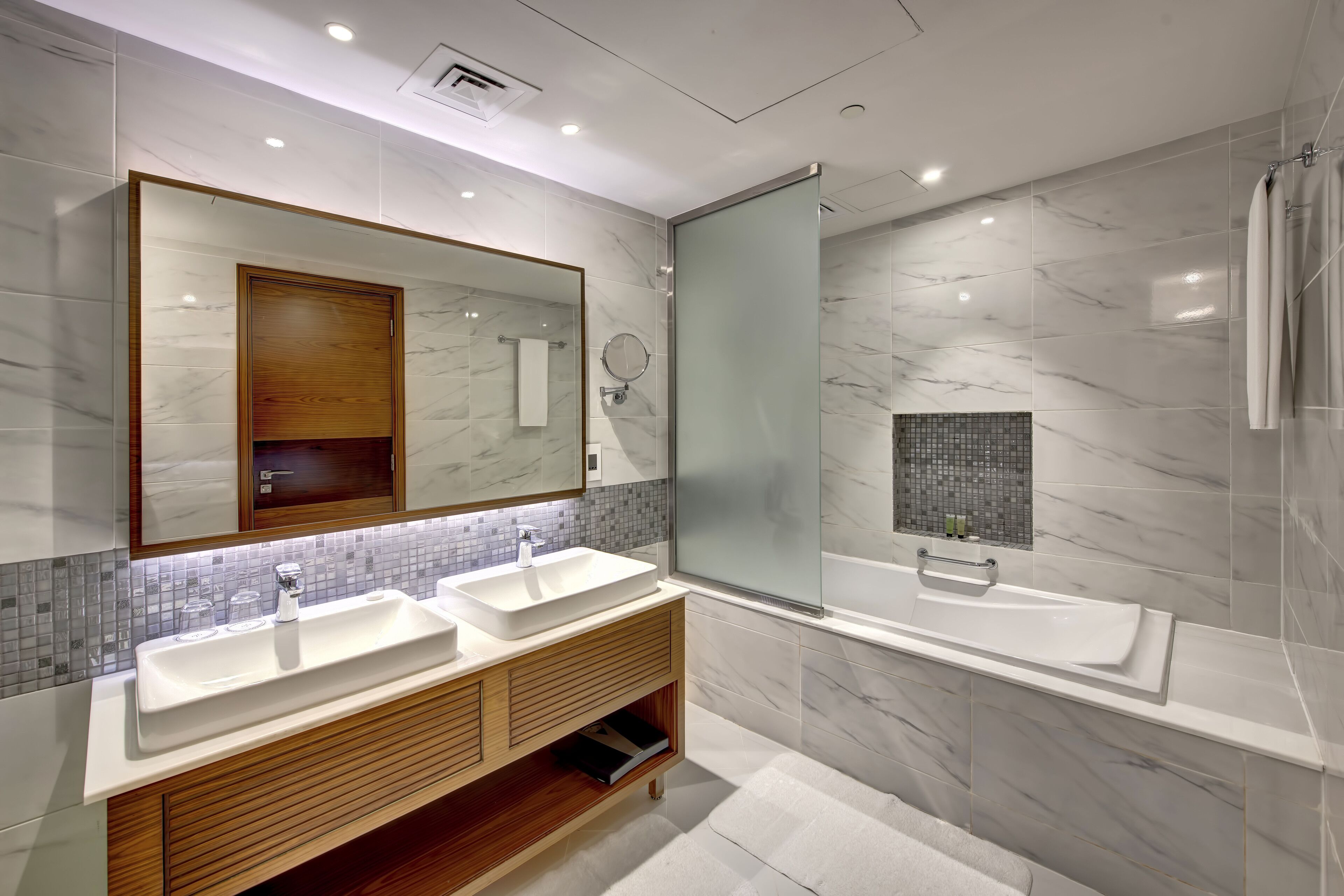 A modern bathroom with two sinks, a large mirror, and a glass-enclosed shower.