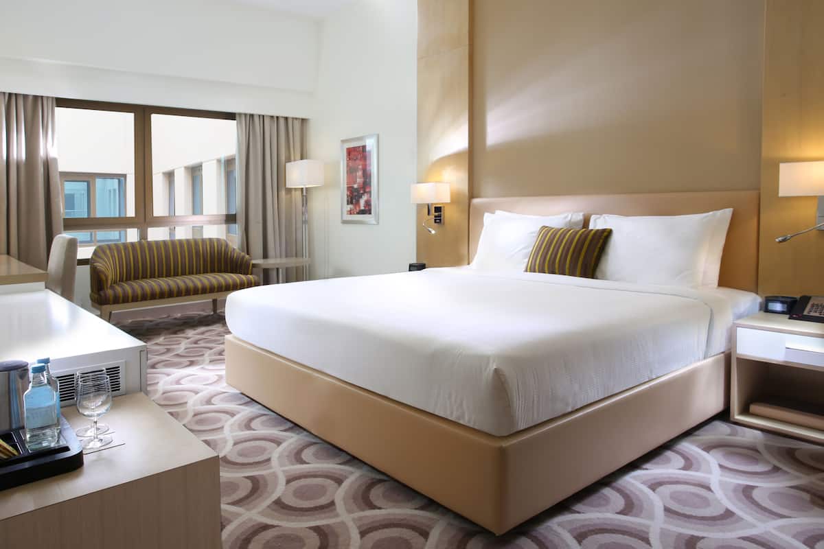 A hotel room with a large bed, a desk with a lamp, a chair, and a window with curtains.