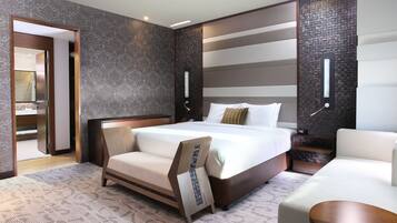 A modern hotel room with a large bed, a sofa, a small table, and a bathroom visible through an open door.