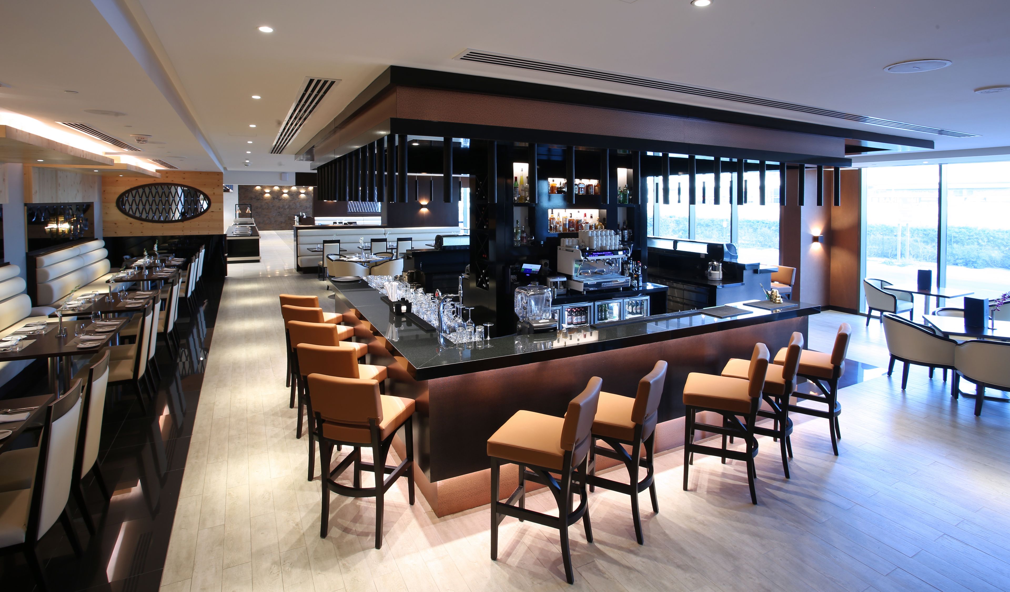 Een moderne bar met een lange toonbank, barstoelen en een groot raam met uitzicht.