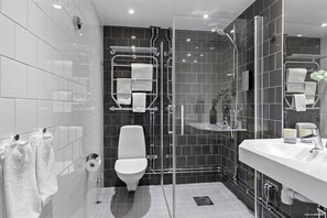 Un baño moderno con ducha de vidrio, inodoro blanco y un lavamanos espacioso con espejo.