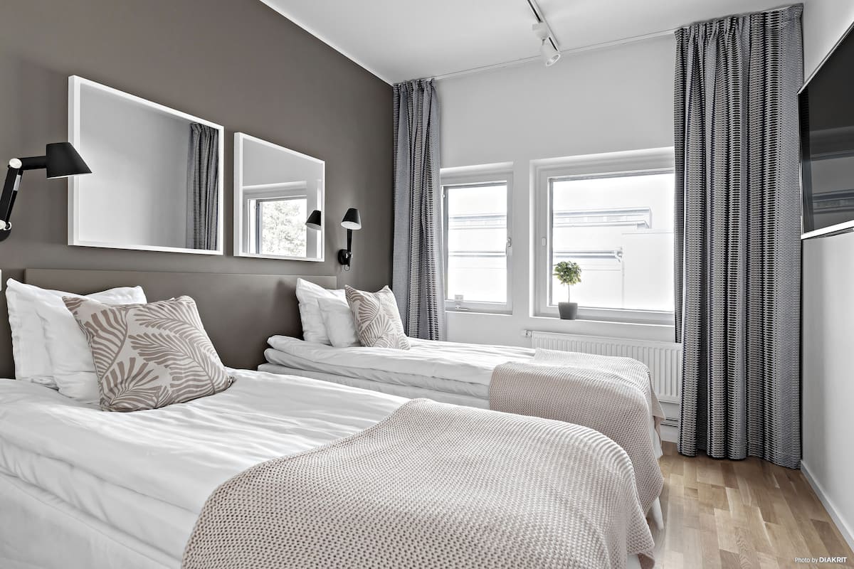 Un dormitorio moderno con dos camas, espejos grandes y un ventanal con cortinas.