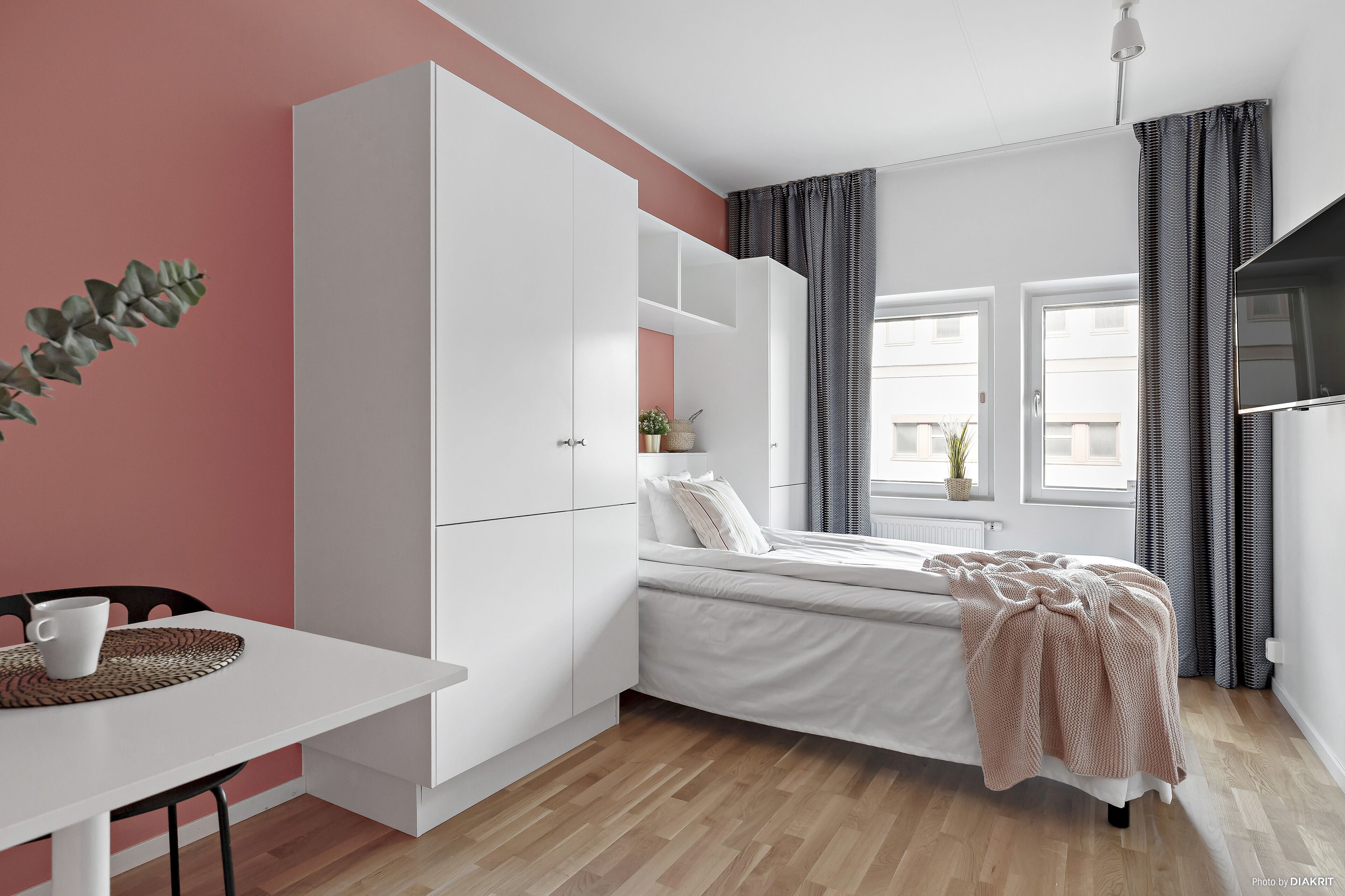Une chambre à coucher de taille modeste, avec un lit, une armoire blanche et une petite table sur laquelle se trouve une tasse.