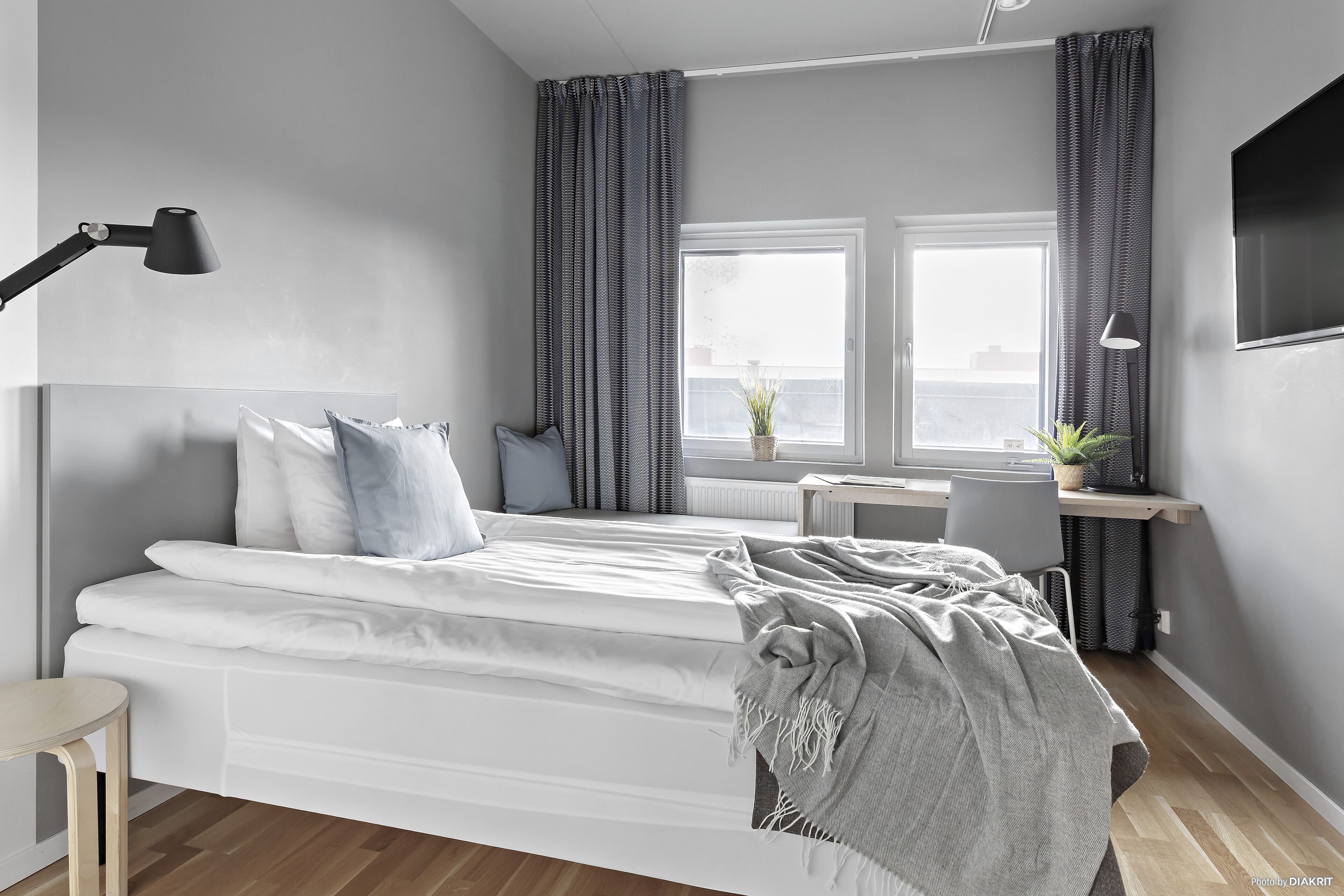 Un dormitorio moderno con cama, lámparas de noche, escritorio y ventana con cortinas.