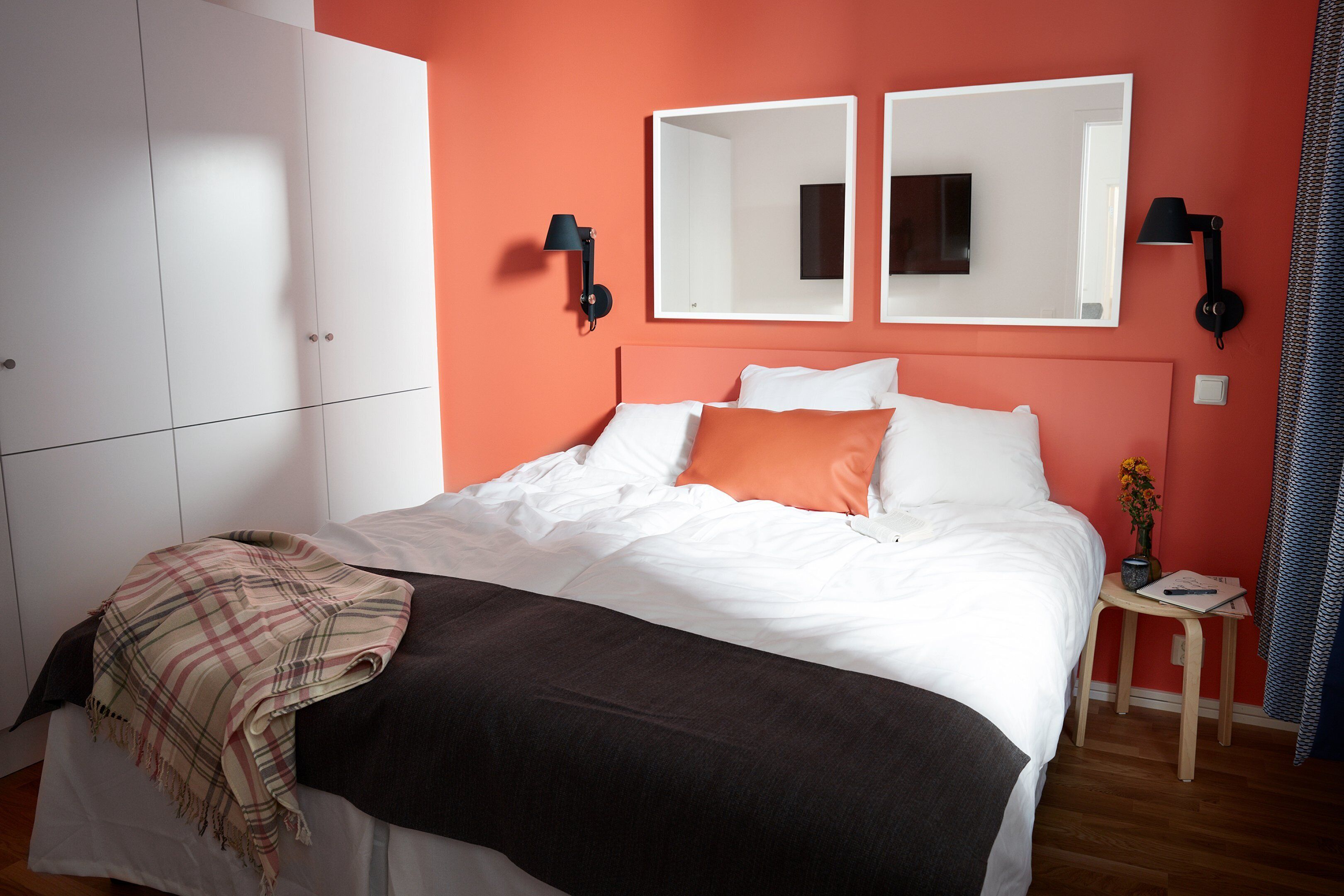 A bedroom with a bed, a bedside table with a lamp, a mirror, and a wardrobe.