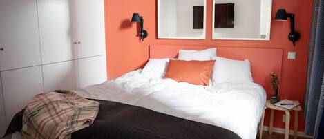 A bedroom with a bed, a bedside table with a lamp, a mirror, and a wardrobe.