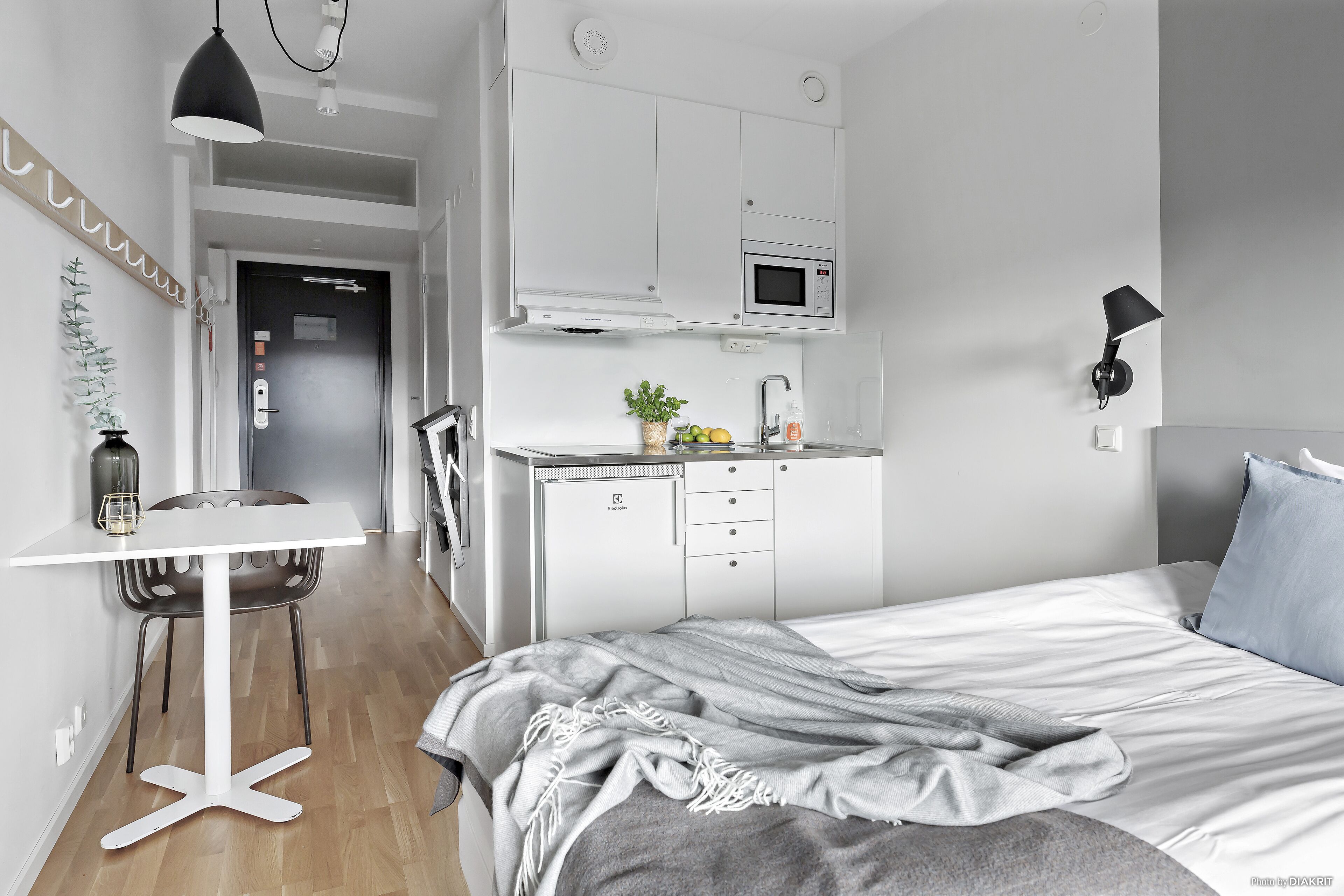 A modern hotel room with a bed, a desk, a chair, a microwave, and a small kitchen area.