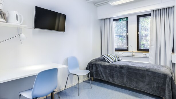 Una stanza con un letto, una scrivania, una sedia, un televisore e il segnale di uscita.