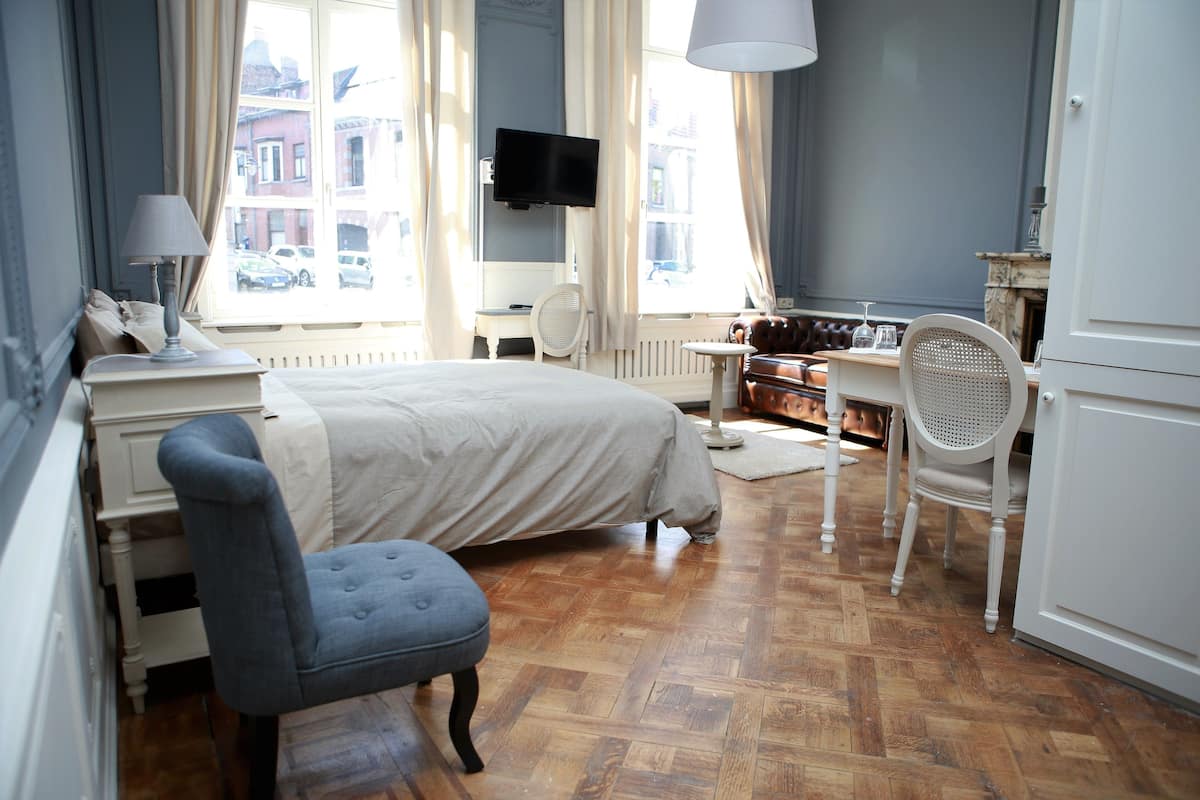 A hotel room with a bed, a desk, a chair, a television, and a view of the street.