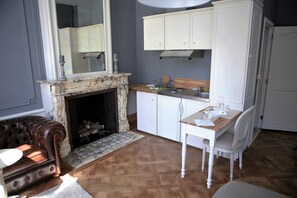 A living room with a fireplace, a dining area with a table and chairs, and a kitchen with white cabinets. - Apart - Hotel Saint Georges (Mons)