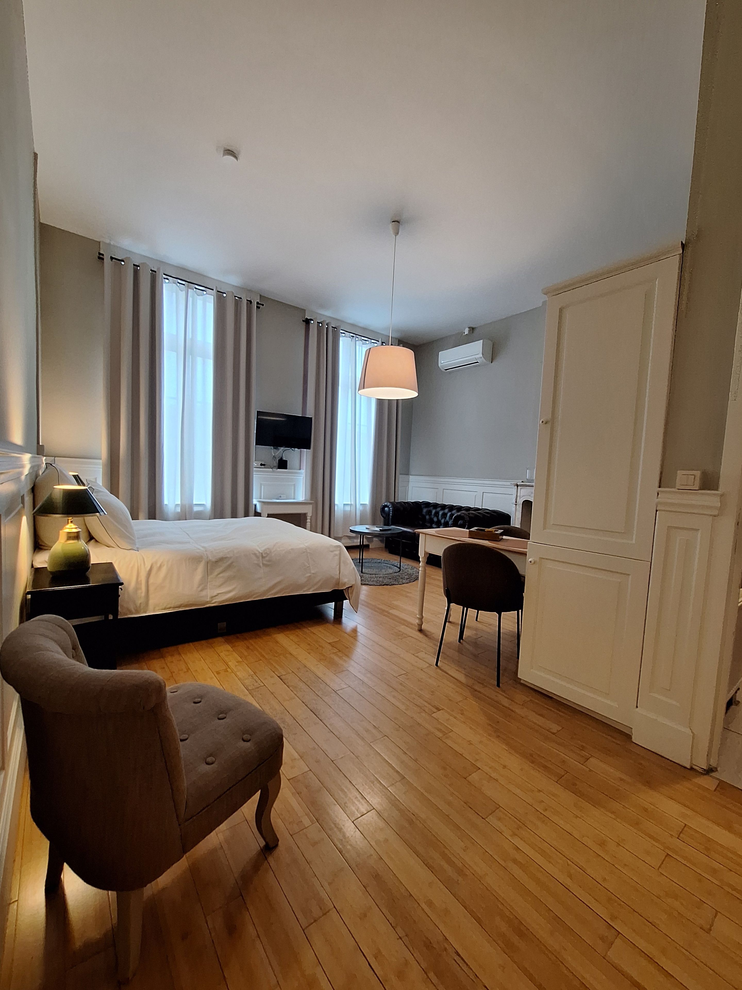 A hotel room with a bed, a desk, a chair, a television, and an air conditioning unit.