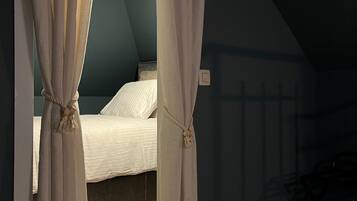 Une chambre à coucher avec un lit, des rideaux attachés en bas, un luminaire au plafond et un plancher en bois.