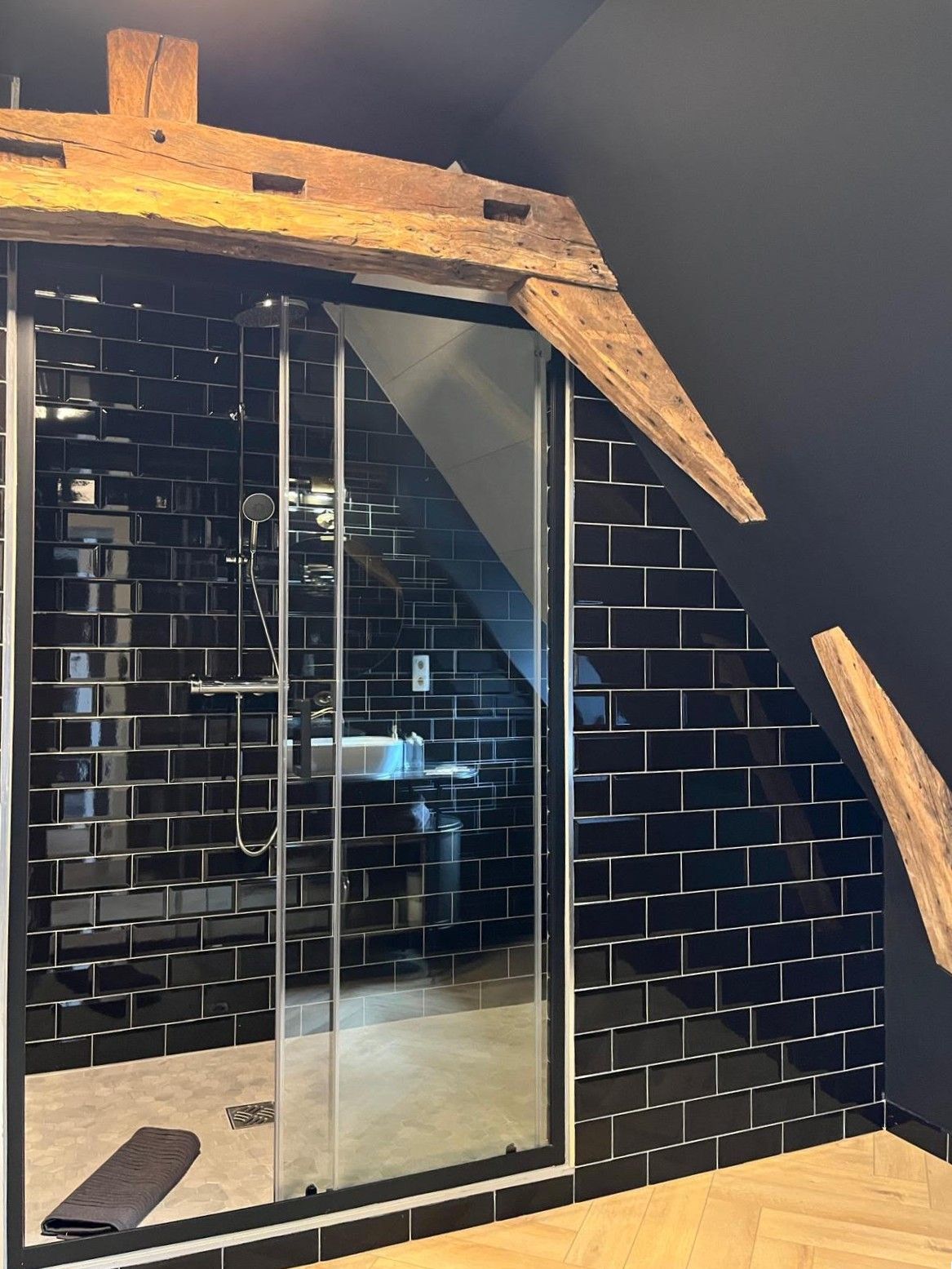 Ein modernes Badezimmer mit schwarzen Fliesen, einer Glasdusche und einer Holzbalkendecke.
