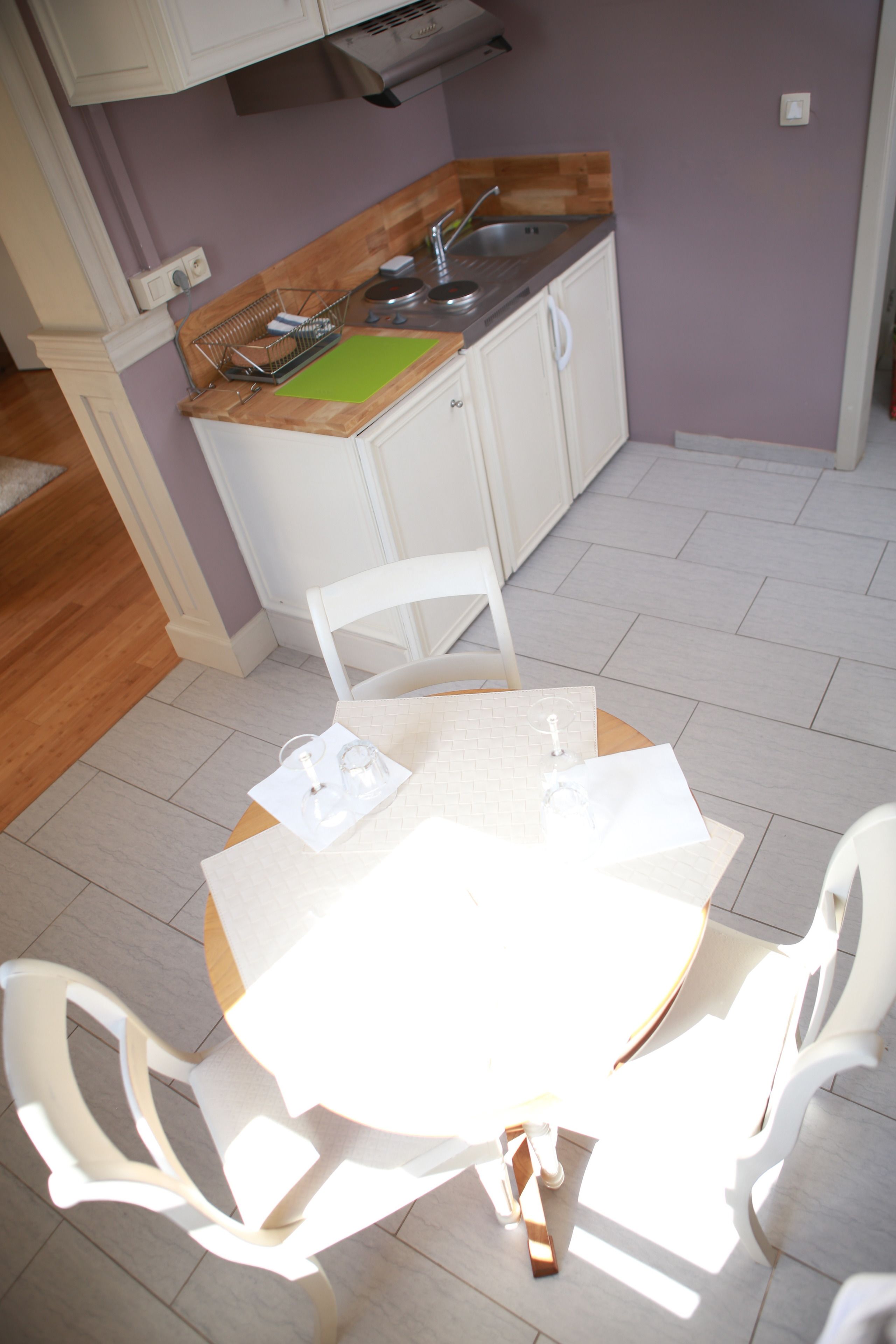 A small kitchen with white cabinets, a wooden countertop, and a sink. There is a table with chairs in the foreground.