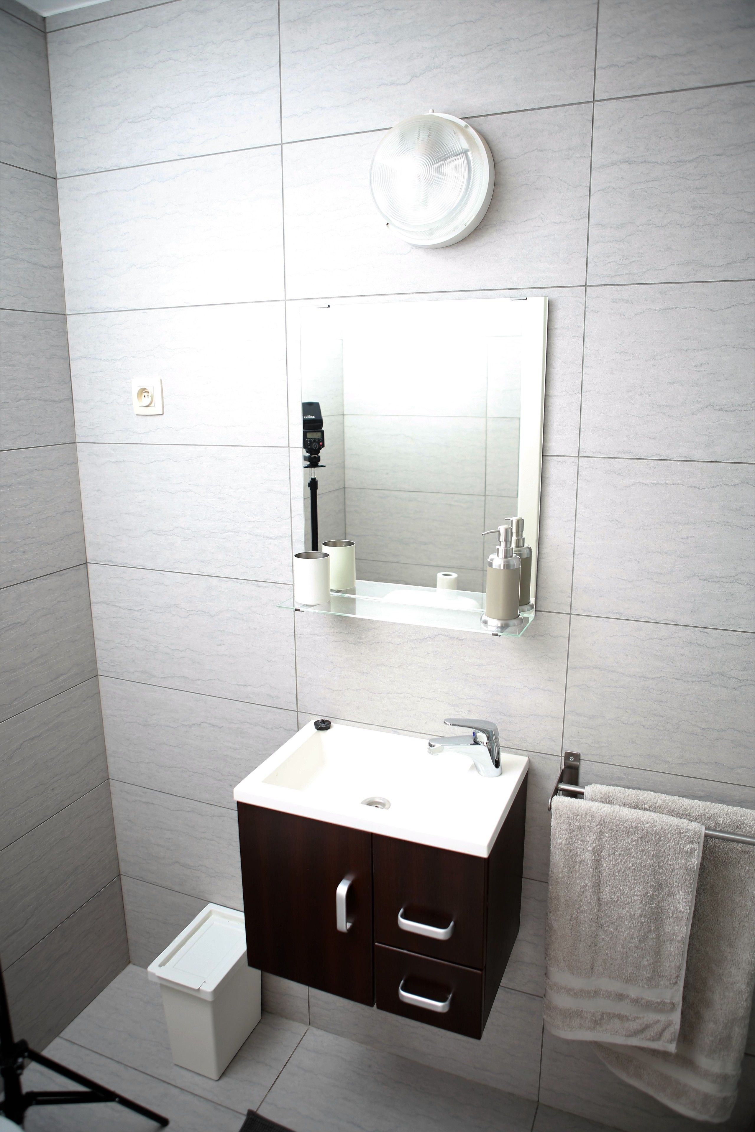 A modern bathroom with a white sink, dark wooden cabinet, and a towel hanging on a rack.