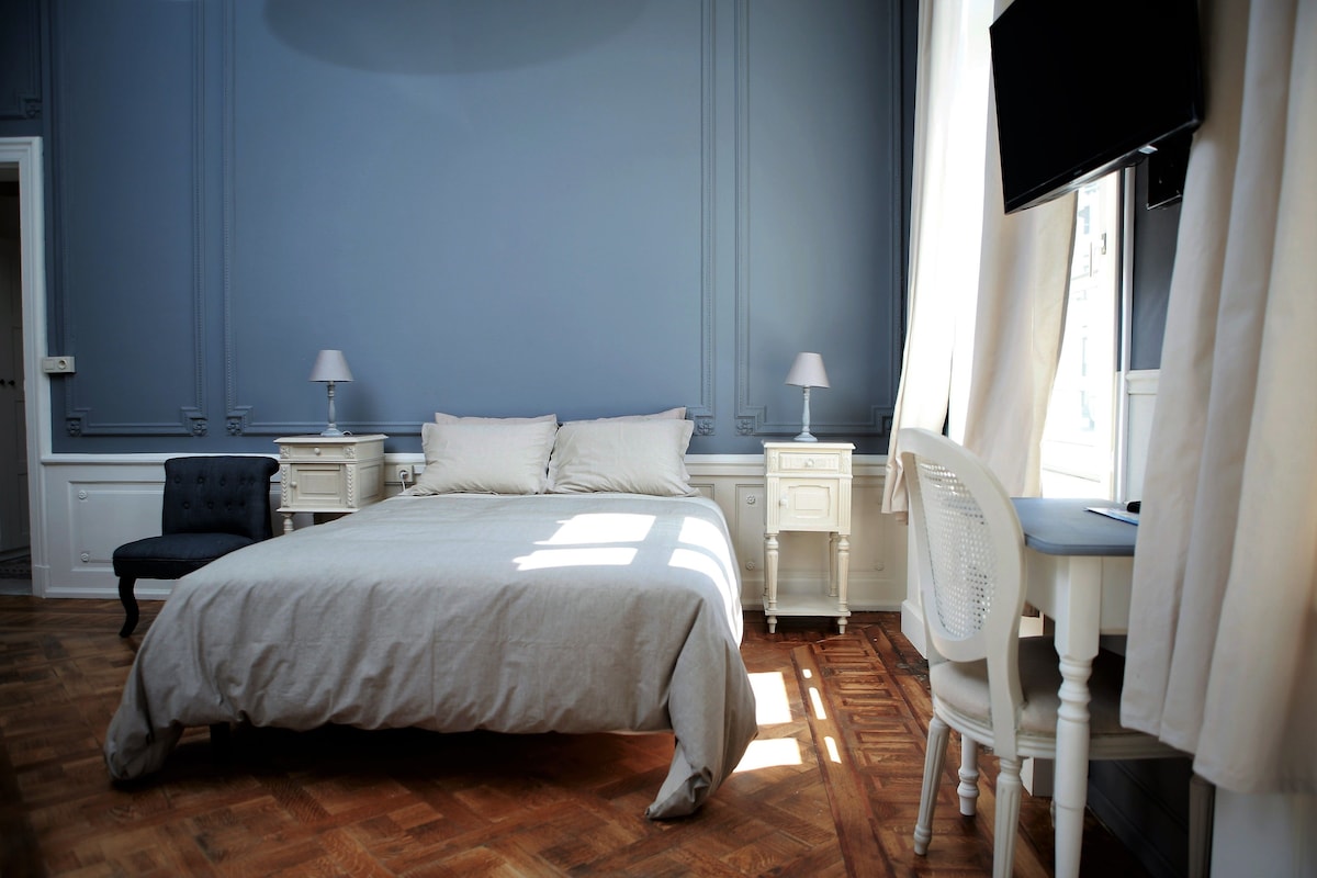 A bedroom with a bed, two bedside tables with lamps, a chair, and a TV mounted on the wall.