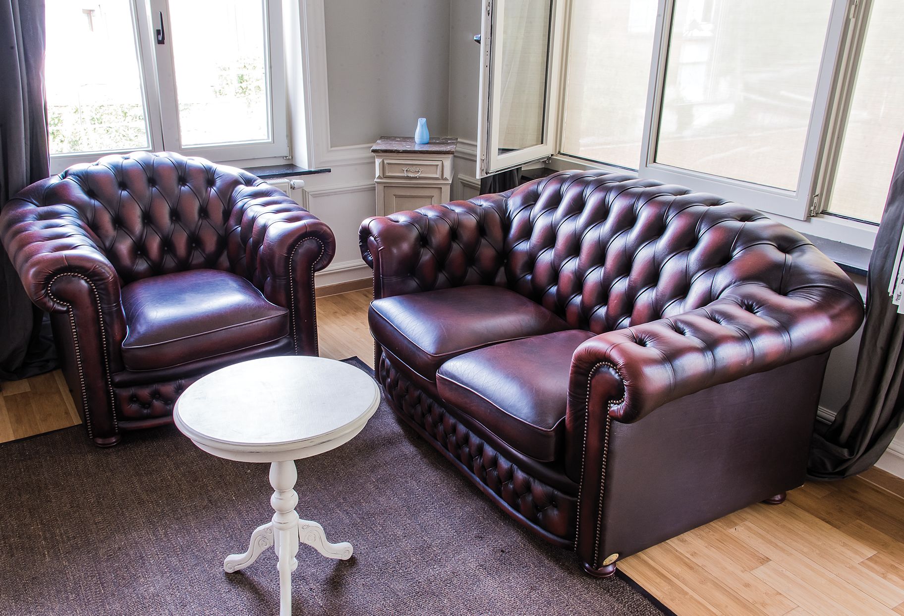 Une pièce avec un canapé et un fauteuil en cuir marron foncé, une table ronde blanche et une vue dégagée grâce à de grandes fenêtres.