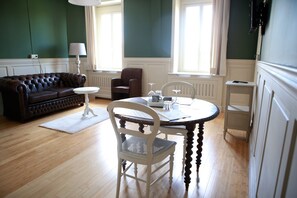 A room with a dark brown leather sofa, a white chair, a small round table, and a lamp. - Apart - Hotel Saint Georges (Mons)