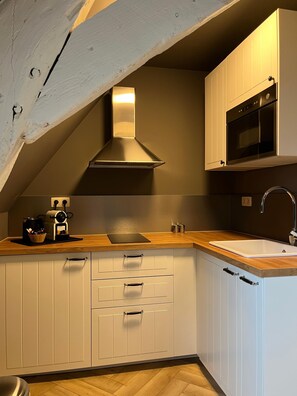 Een keuken met witte kasten, een roestvrijstalen afzuigkap, een magnetron en een houten aanrecht.