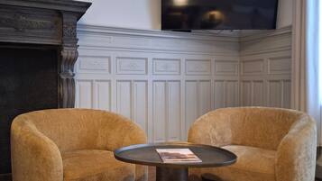 Une pièce comprenant deux fauteuils, une table ronde, une cheminée et un téléviseur fixé au mur.