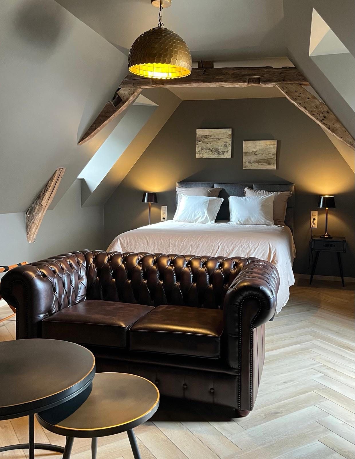 Une chambre à coucher avec un lit, un canapé en cuir, une table ronde et un luminaire suspendu.
