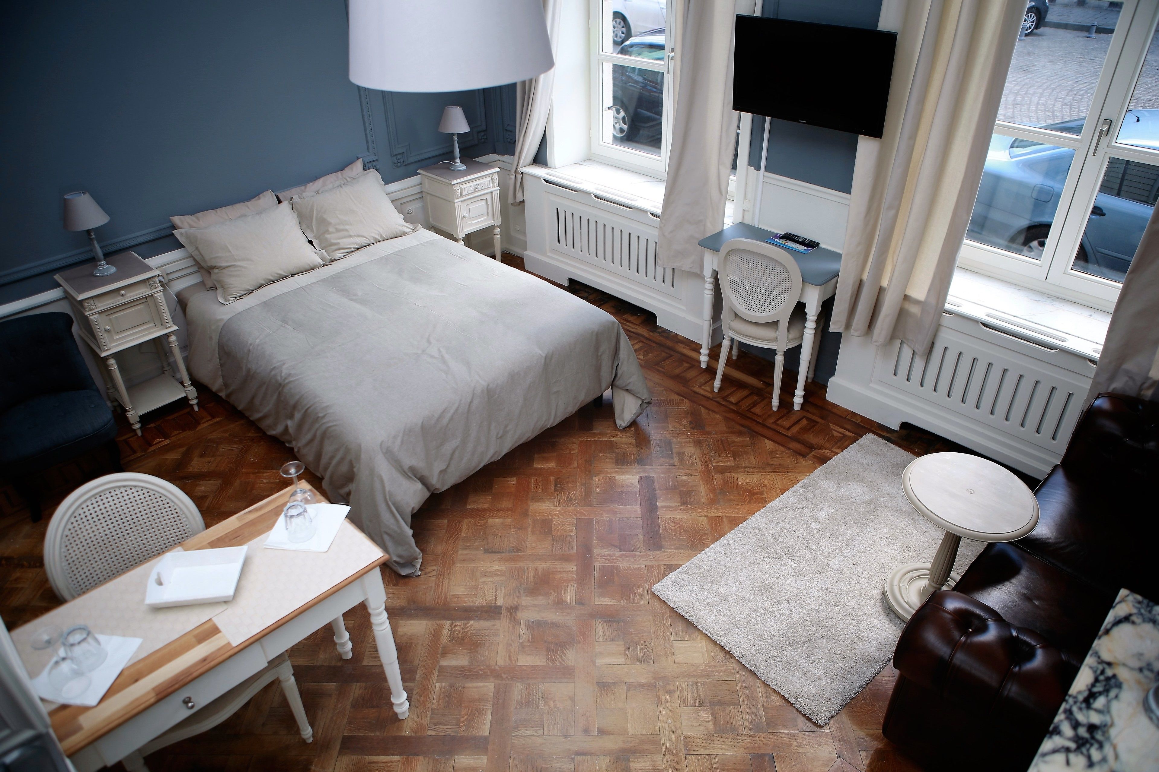 Een slaapkamer met een bed, nachtkastjes, een bureau, een stoel, een klein tafeltje en een raam met gordijnen.