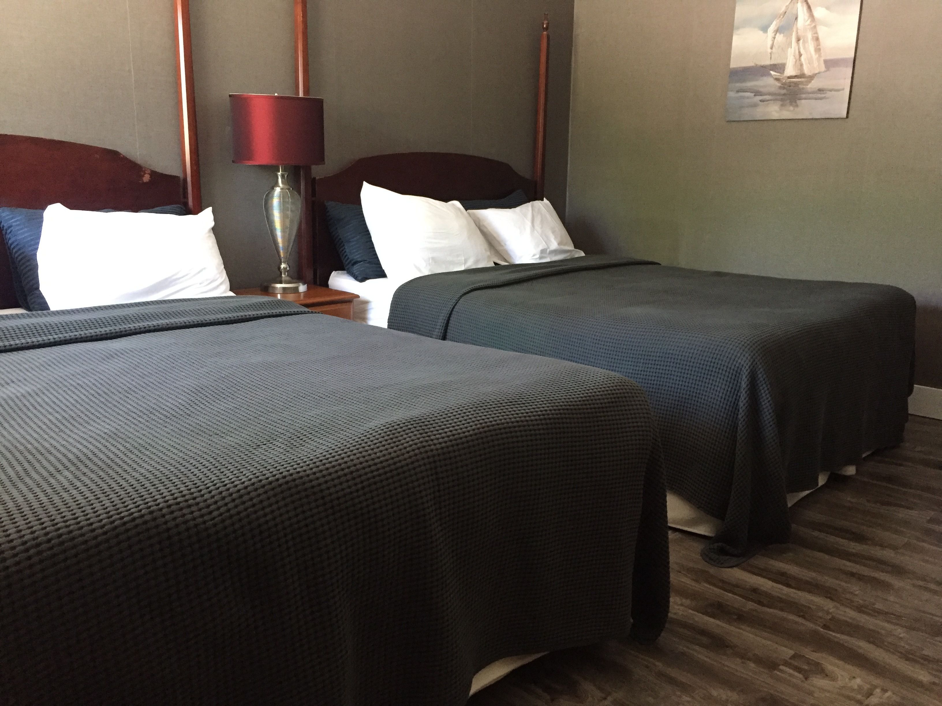 Habitación de hotel con dos camas, una mesita de noche con una lámpara y un cuadro en la pared.