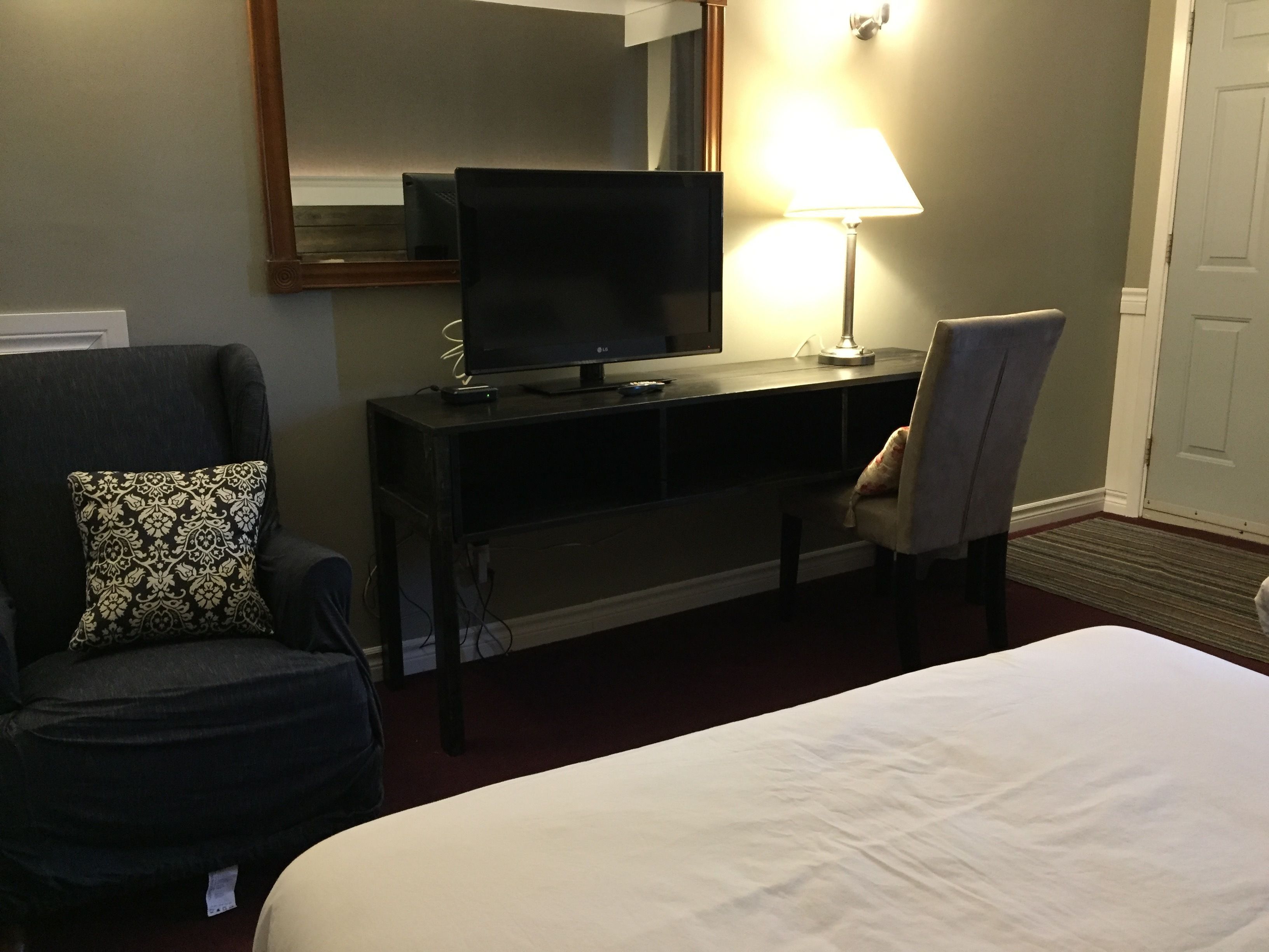A hotel room with a bed, a desk with a TV, a chair, and a lamp.