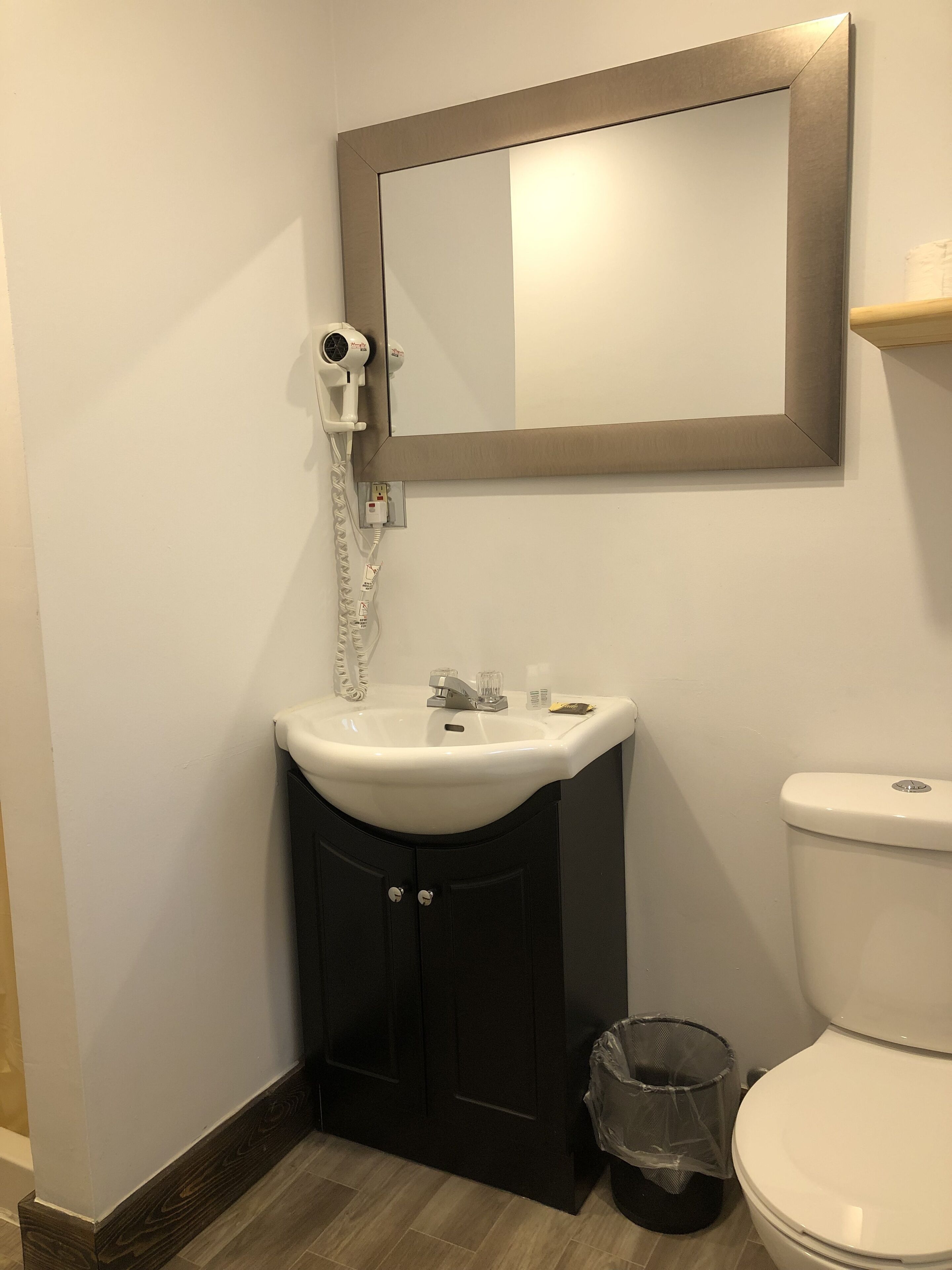 A bathroom with a white sink, dark cabinets, a mirror, and a toilet.