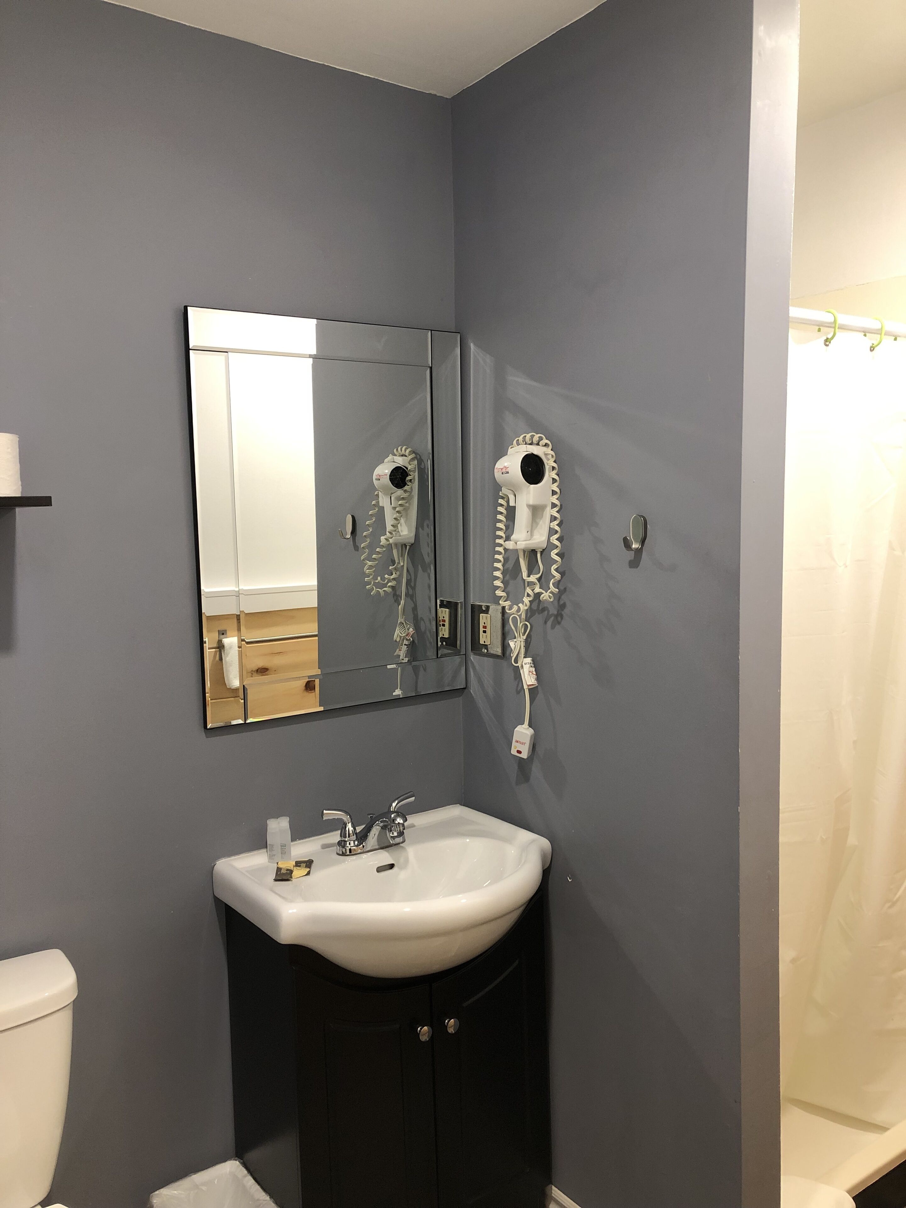A bathroom with a sink, mirror, and two hair dryers mounted on the wall.