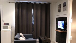 Una habitación de hotel con una cama, un sofá, un televisor, una mesita y un microondas.