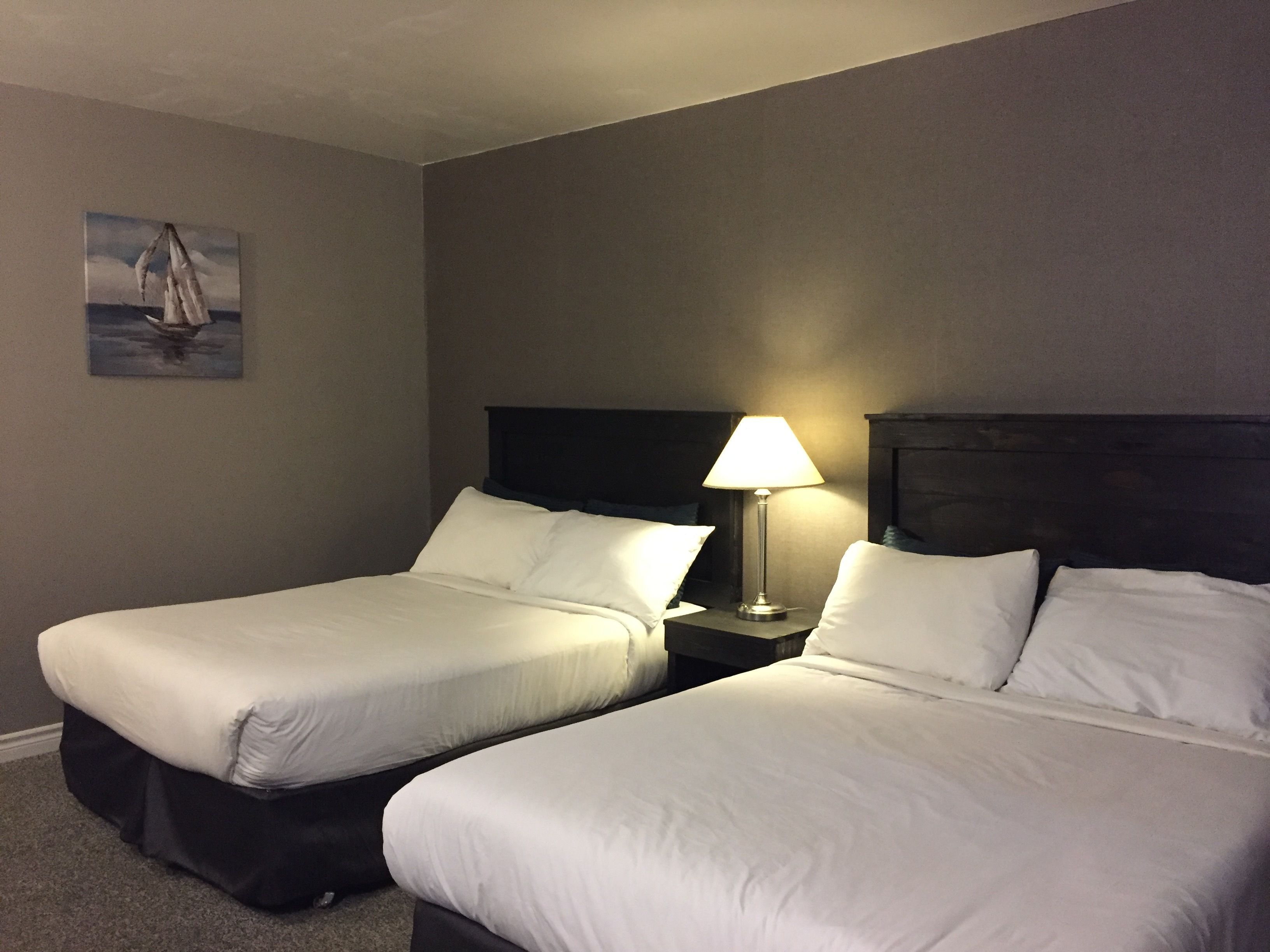 A hotel room with two single beds, a nightstand with a lamp, and a painting on the wall.