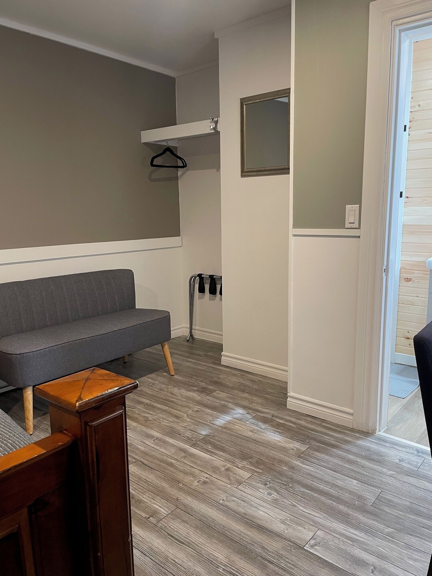 Una habitación con un sofá gris, una mesita de madera, un perchero y una puerta que da a otra estancia.