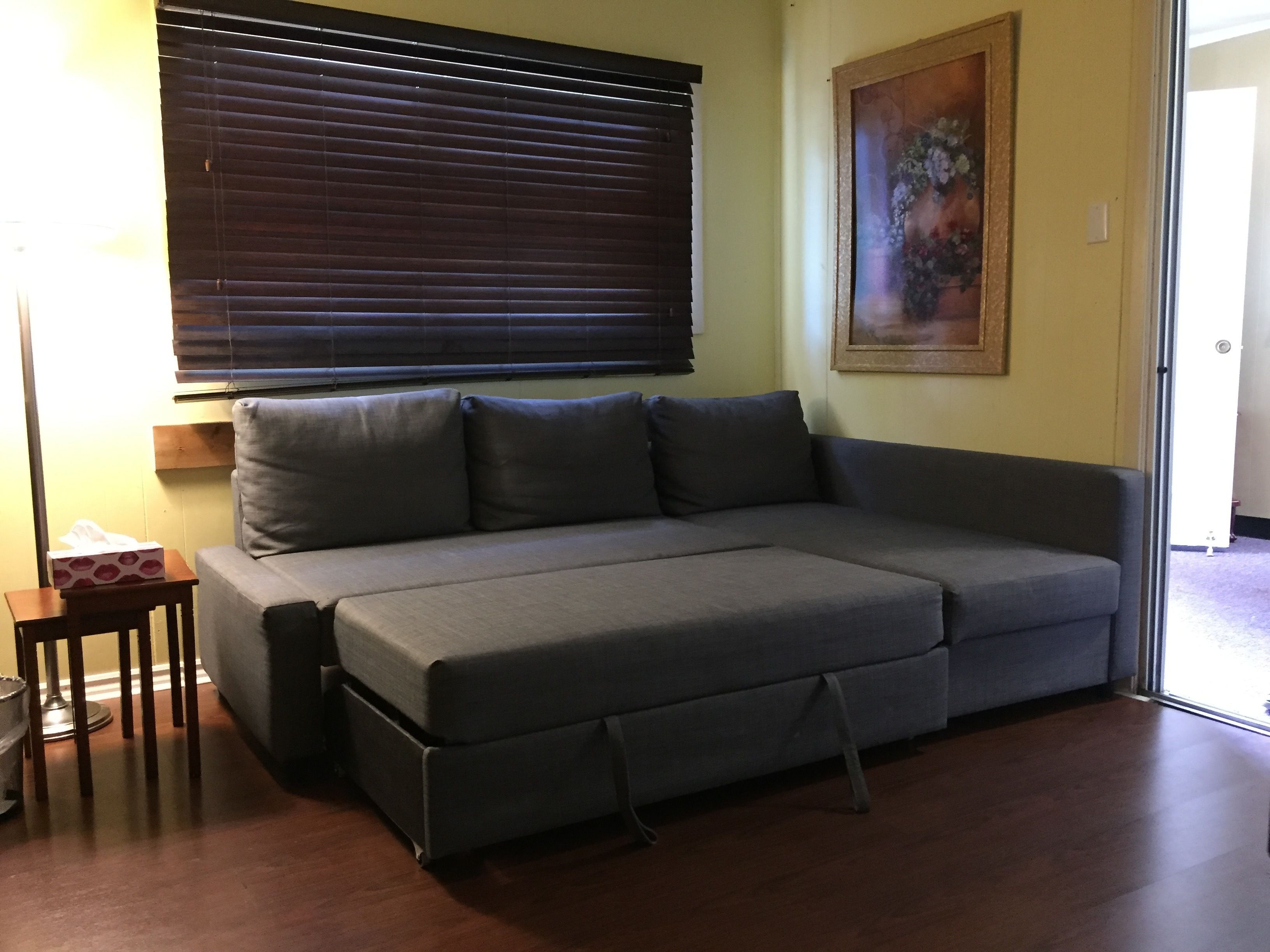 A grey sofa with a footrest, a small wooden side table, a lamp, and a painting on the wall.