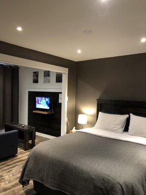 A hotel room with a large bed, a TV mounted on a dark wall, a small table, and a chair. - Greenside motel (St. Andrews)