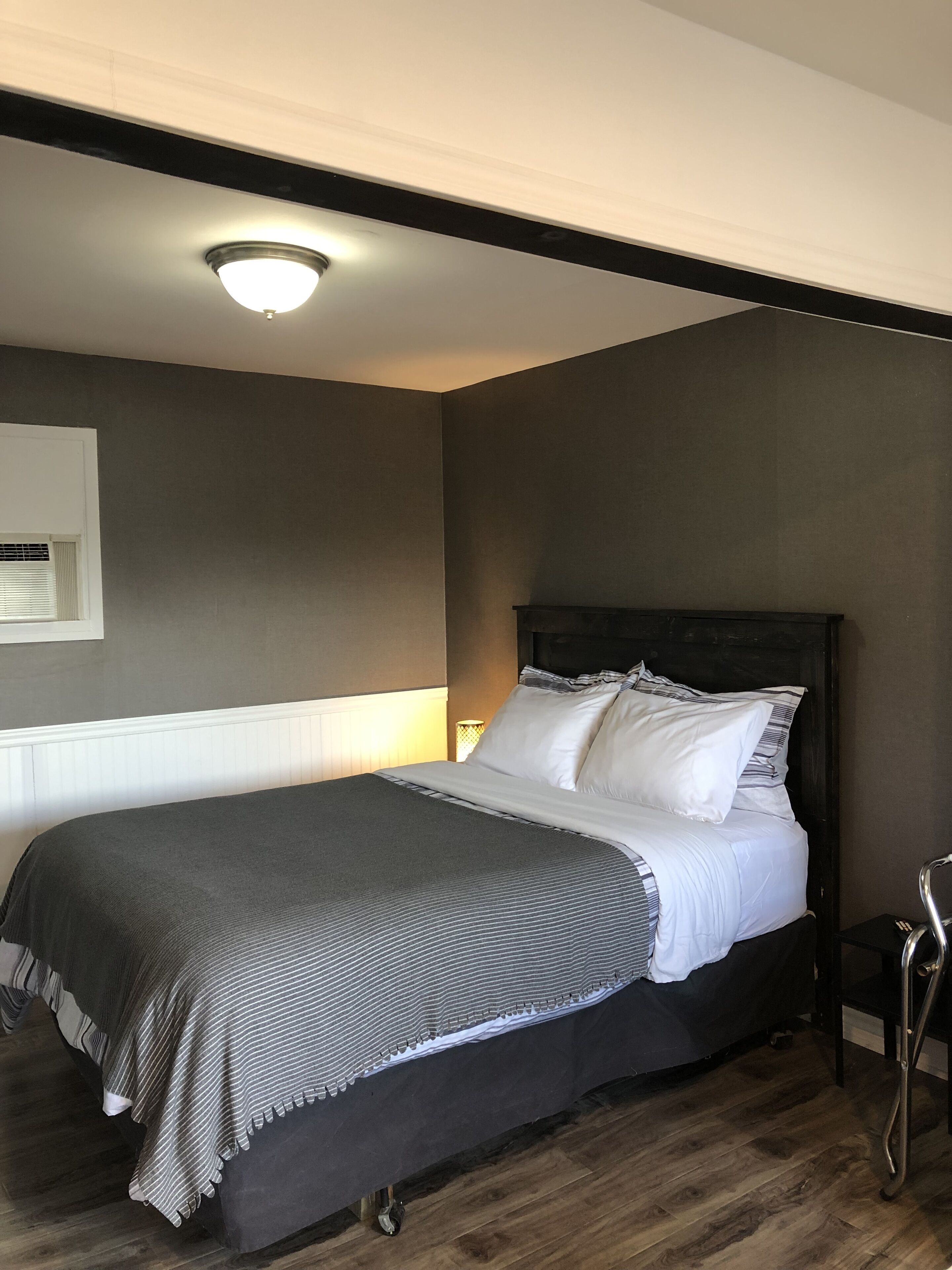 Una cama bien hecha con un cabecero oscuro y ropa de cama blanca, una lámpara de noche y suelo de madera.