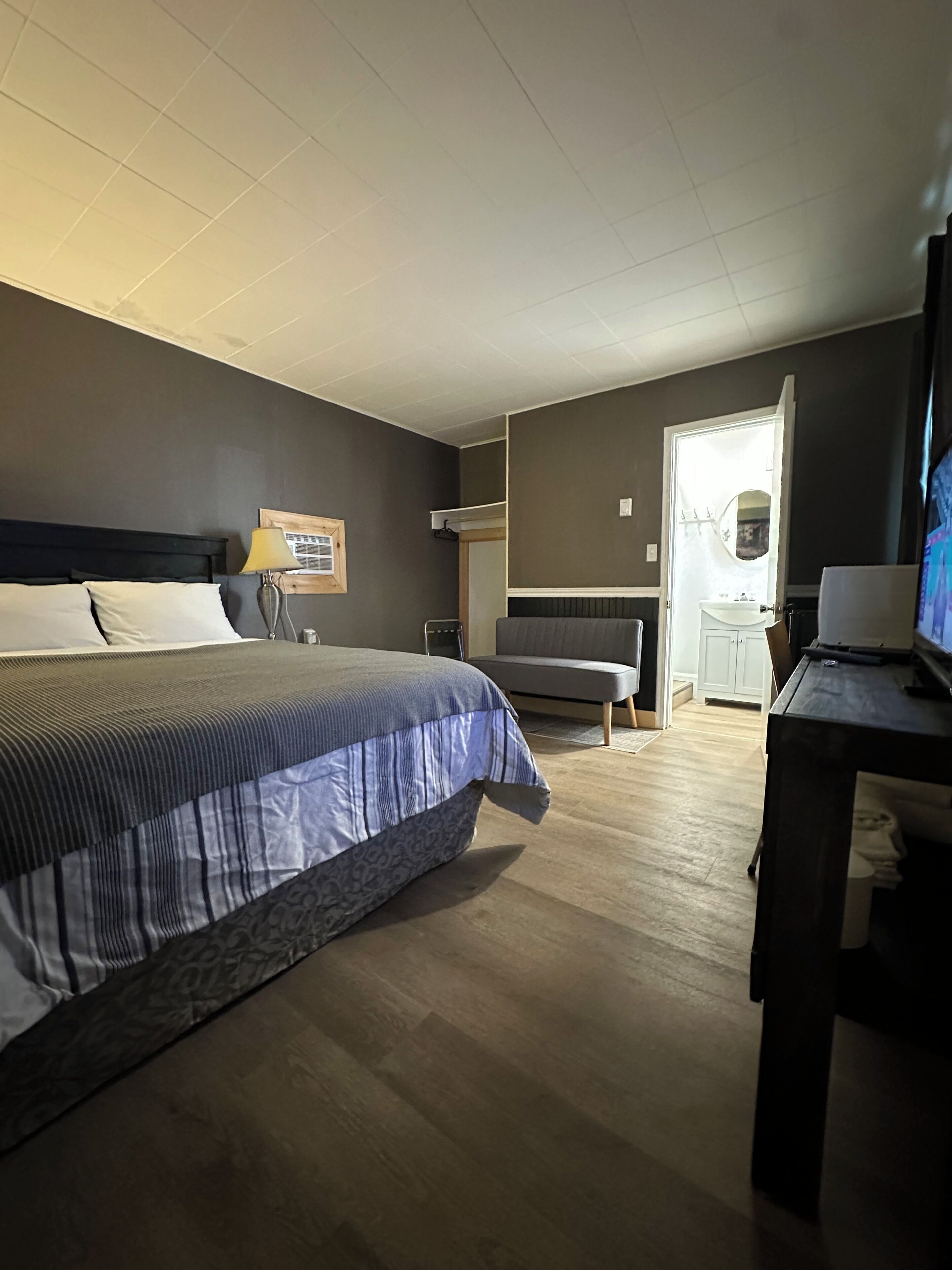 A hotel room with a bed, a desk, a chair, a television, and a bathroom visible through an open door.