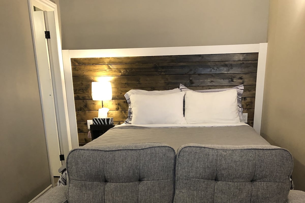A modern bedroom with a grey upholstered sofa, a wooden headboard, and a bedside table with a lamp.