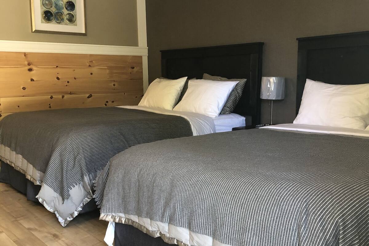 A hotel room with two beds, wooden headboards, and a framed artwork on the wall.