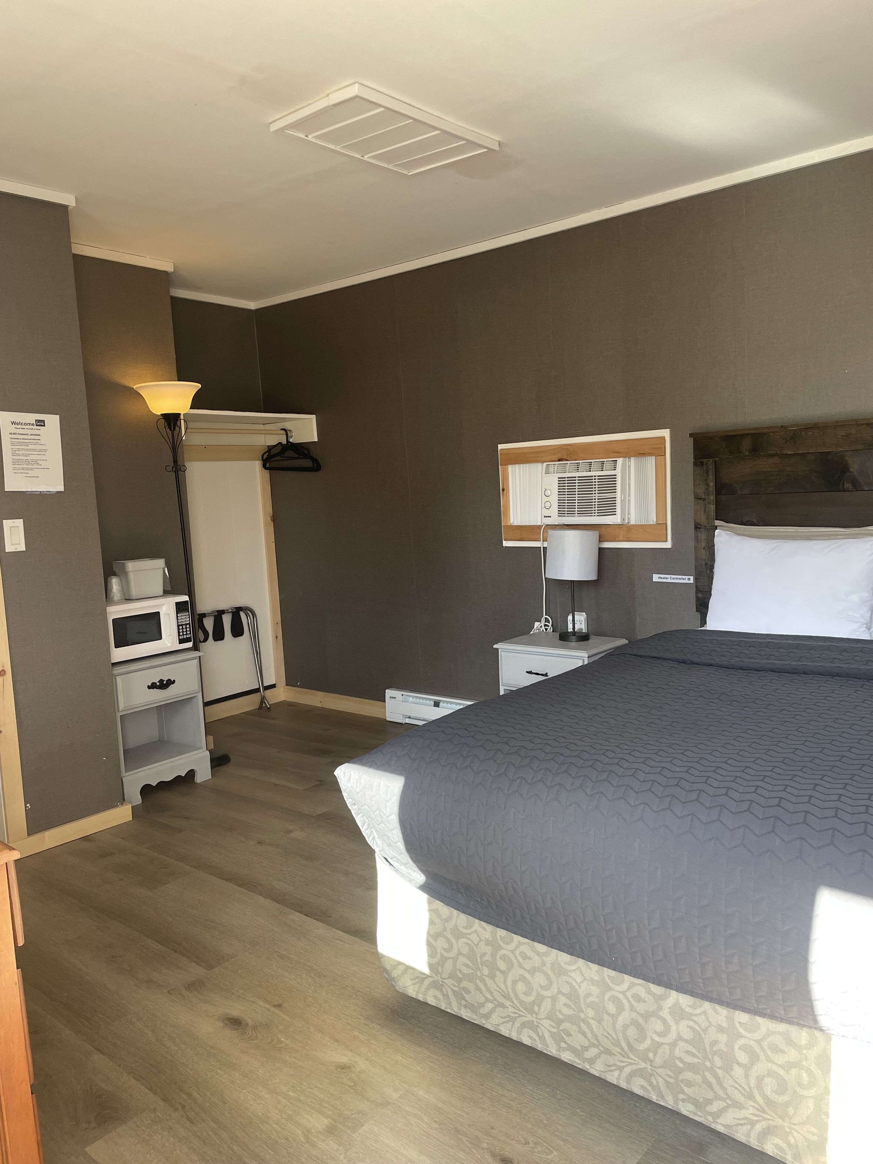 A hotel room with a bed, bedside tables, a lamp, a microwave, and a heater.