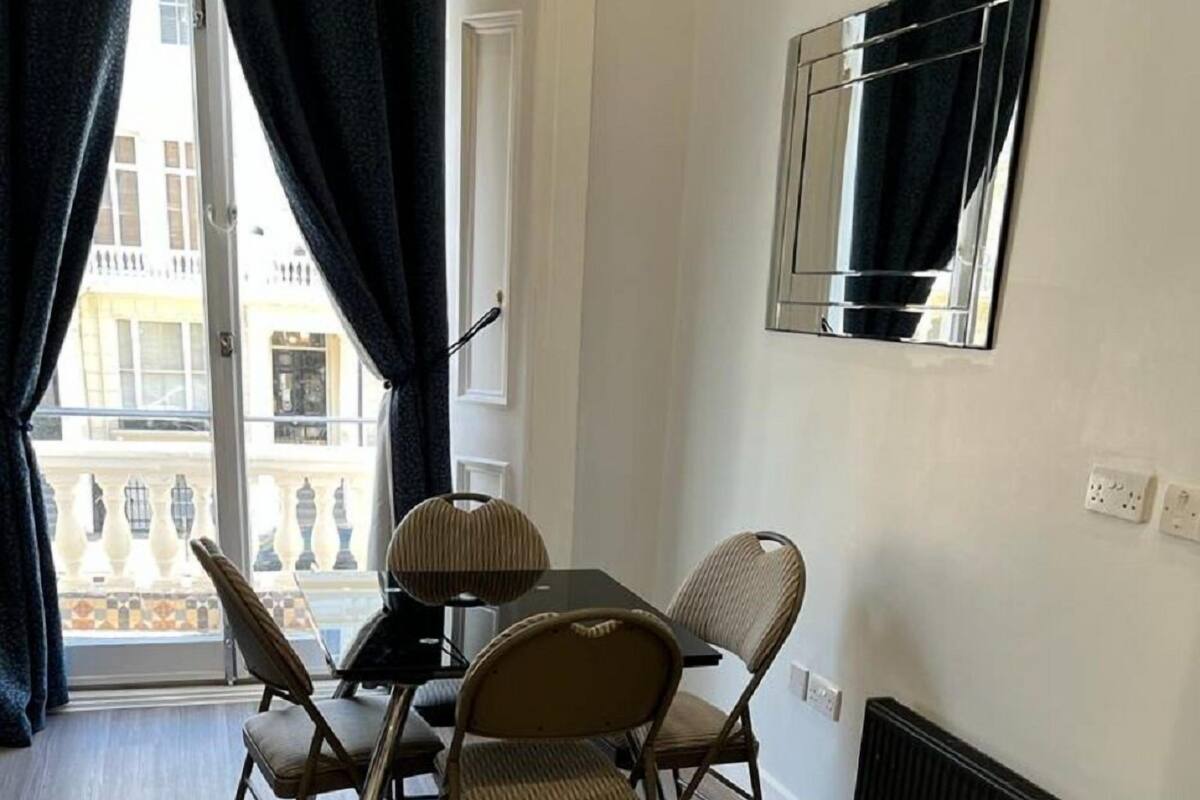 A dining area with a table and chairs, a window with curtains, a radiator, and a wall-mounted mirror.
