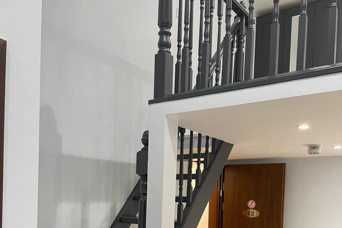 A modern staircase with black railings and a wooden door with a number plate.