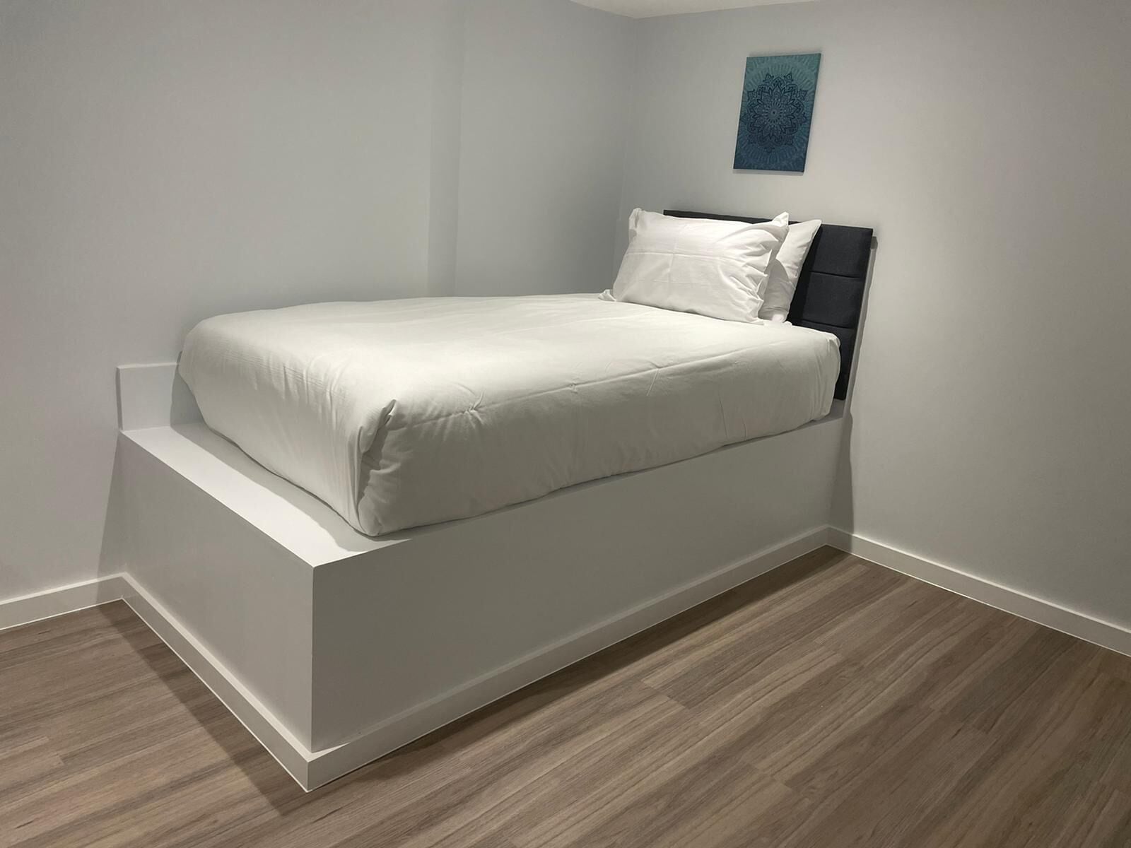 A modern, minimalist bedroom with a single bed, a small bedside table, and a wall-mounted artwork.