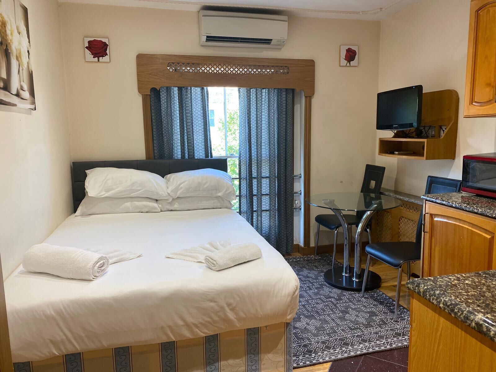 A hotel room with a bed, a desk, a TV, and an air conditioning unit.