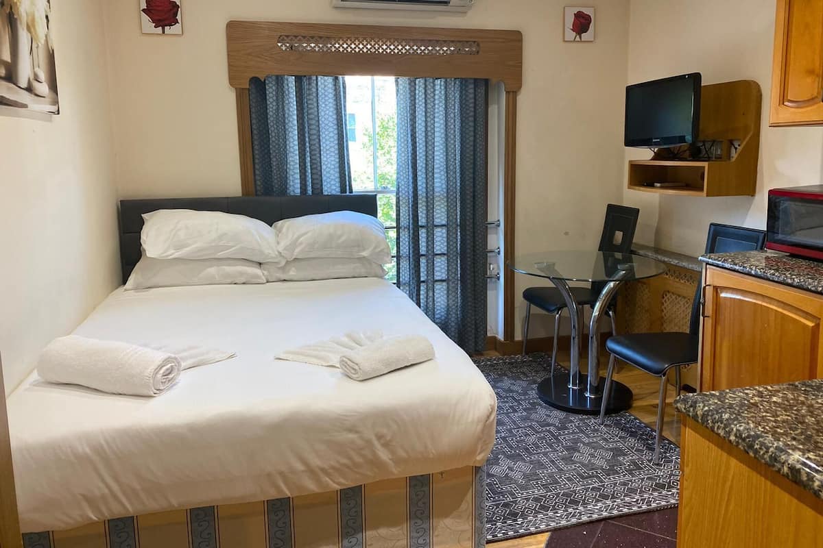 A hotel room with a bed, a desk, a TV, and an air conditioning unit.