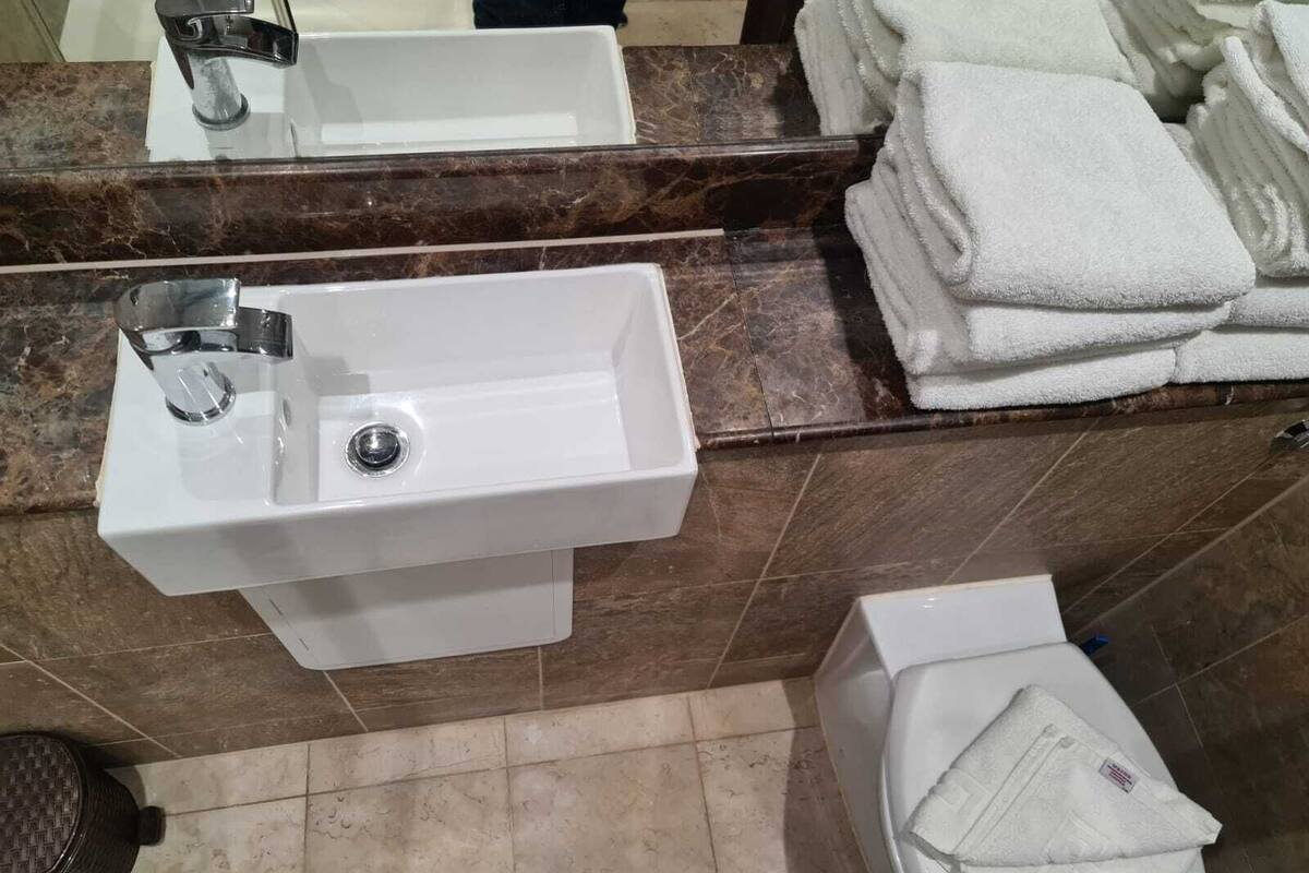 A bathroom with a white sink, a toilet, and a stack of white towels.