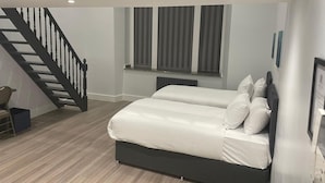 Un dormitorio con una cama, un ventanal con cortinas, una escalera y un radiador.