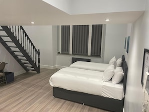 A bedroom with a bed, a window with curtains, a staircase, and a radiator. - MSK Superior (London)