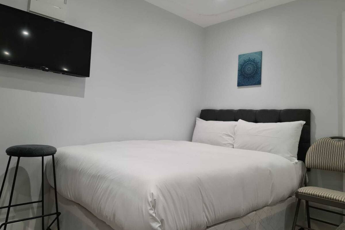 A modern bedroom with a large bed, a flat-screen TV mounted on the wall, and a small stool.